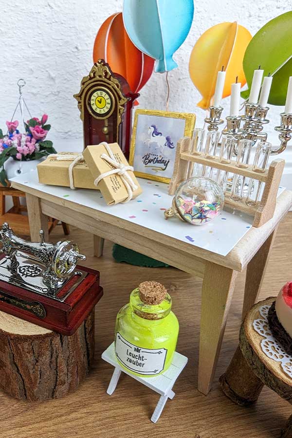 Bunte Wichteldekoration im Regenbogen-Design mit Mini-Girlande, farbenfrohen Geburtstagsaccessoires und Wichteltür im Hintergrund.